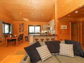 An open plan wooden interior with a kitchen island with bar stools a dining table with chairs and a sofa with cushions at Forsa Lodge in Glenforsa near Salen Isle Of Mull