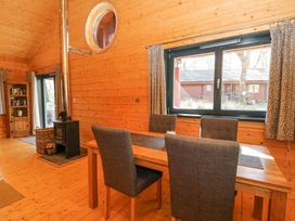 A dining area with a wooden table and four chairs next to a window and a wood stove in a wooden cabin at Forsa Lodge in Glenforsa near Salen Isle Of Mull
