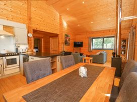An open plan wooden cabin interior with a dining table and chairs a kitchen area with appliances and a living area with sofas a wood burning stove and a window at Forsa Lodge in Glenforsa near Salen Isle Of Mull