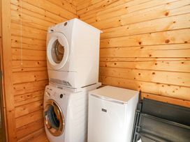 A laundry room with a stacked washer and dryer and a small white refrigerator against wooden walls at Forsa Lodge Glenforsa near Salen Isle Of Mull