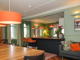 A dining area with wooden tables and chairs a bar with orange stools and orange pendant lights and a grey sofa with cushions at Sycamore Apartment in Lifton