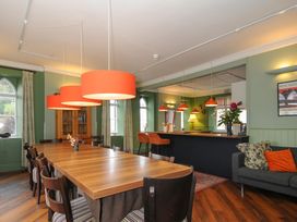 A dining area with a long wooden table and chairs under orange pendant lights next to a bar counter and sofa at Sycamore Apartment in Lifton
