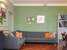 A living room with a grey sectional sofa and orange and floral cushions against a green wall with framed artwork and a dining area visible through an open door at Sycamore Apartment in Lifton