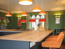 A kitchen island with orange chairs and pendant lights in a green walled room at Sycamore Apartment in Lifton
