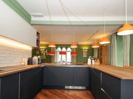 A kitchen with black cabinets wooden countertops orange hanging lights and green walls at Sycamore Apartment in Lifton