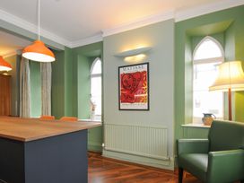 A room with green walls featuring two arched windows a green armchair a wooden table with orange chairs and orange pendant lights at Sycamore Apartment in Lifton