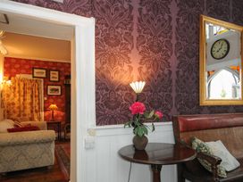 A room with patterned wallpaper a small round table with flowers a wall lamp and a wooden bench with cushions at Sycamore Apartment in Lifton