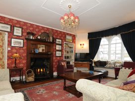 A living room with armchairs a fireplace a wooden coffee table a wall with framed pictures and a window seat with cushions at Sycamore Apartment in Lifton