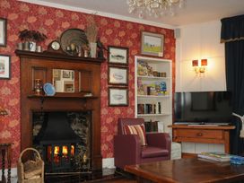 A living room with a wooden fireplace with fire a bookshelf a television on a wooden stand and a red armchair at Sycamore Apartment in Lifton
