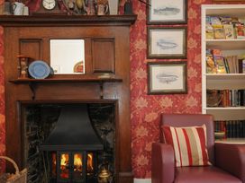 A room with a wooden fireplace with fire burning a red chair with a striped pillow and framed fish illustrations on the wall at Sycamore Apartment in Lifton