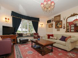 A living room with a large window with blue curtains a wooden coffee table a patterned sofa and paintings on the wall at Sycamore Apartment in Lifton