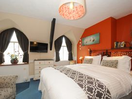 A bedroom with a large bed two windows with dark curtains a chest of drawers and a wall-mounted TV at Sycamore Apartment Lifton