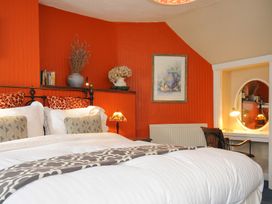 A bedroom with a bed against an orange wall with decorative pillows and a shelf with vases and books at Sycamore Apartment in Lifton