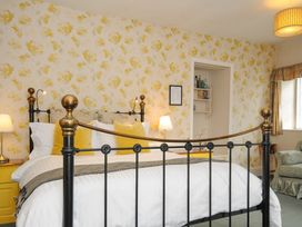 A bedroom with a metal bed frame yellow pillows bedside tables lamps floral wallpaper and an armchair at Sycamore Apartment in Lifton