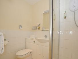 A bathroom with a toilet, sink, mirror, glass shelf with cups, towel holder, and a shower at Sycamore Apartment in Lifton