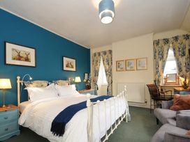 A bedroom with a double bed blue accent wall floral curtains bedside tables lamps and a seating area at Sycamore Apartment in Lifton