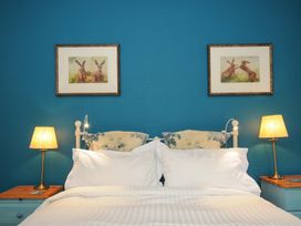 A bedroom with a bed with white pillows and sheets two bedside tables with lamps and framed pictures on a blue wall at Sycamore Apartment in Lifton