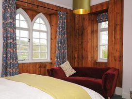 A bedroom with a bed a burgundy sofa wooden paneled walls and arched windows with patterned curtains at Sycamore Apartment in Lifton