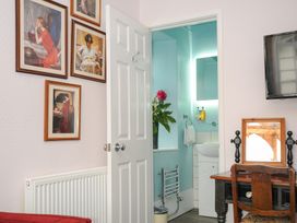 A room with framed paintings on the wall a wooden desk and chair a television and an open door showing a bathroom with a vase of flowers at Sycamore Apartment in Lifton