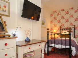 A bedroom with floral wallpaper a metal bed a wooden desk with a blue vase and a wall-mounted television at Sycamore Apartment in Lifton