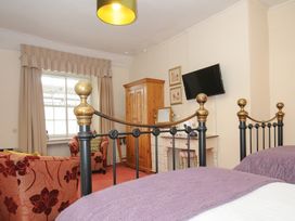 A bedroom with a metal bed frame purple bedding a wooden wardrobe armchair and a wall-mounted television at Sycamore Apartment in Lifton