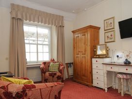 A room with two upholstered armchairs near a window and a wooden wardrobe next to a white desk with a framed mirror and a small striped stool