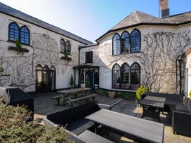 An outdoor patio area with wooden picnic table and wicker furniture outside a white building with arched windows at Sycamore Apartment in Lifton