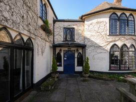 An exterior courtyard with a blue door flanked by two planters and a building with arched windows at Sycamore Apartment in Lifton