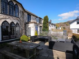 An outdoor patio with wooden picnic table and black sofa seating outside a building with arched windows at Sycamore Apartment in Lifton