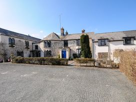 A white building with arched windows and a blue door surrounded by hedges and a paved parking area at Sycamore Apartment in Lifton