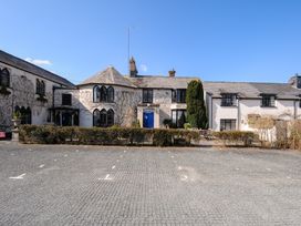 A stone paved parking area in front of a white building with arched windows and blue doors at Sycamore Apartment in Lifton