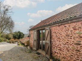 An exterior view of a stone building with wooden doors open on a gravel ground with trees in the background at The Barn in Spaxton