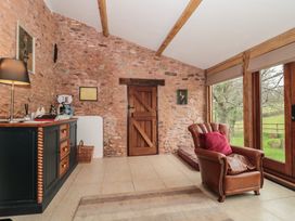 A room with a leather armchair a wooden sideboard and a wooden door with stone walls and large windows showing a garden at The Barn in Spaxton