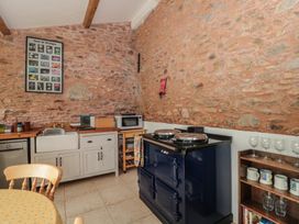 A kitchen with a stone wall, sink, microwave, stove, wooden chairs and shelves with cups and glasses at The Barn in Spaxton