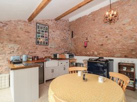 A kitchen with stone walls a round table with chairs and a stove at The Barn in Spaxton