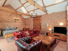 A room with a bed a wooden desk a red sofa a black armchair a wooden coffee table a television and stone walls at The Barn in Spaxton