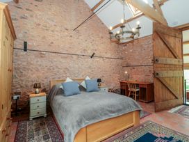 A bedroom with a double bed two pillows bedside tables lamps a wooden wardrobe a desk and chair exposed stone walls and a wooden door at The Barn in Spaxton