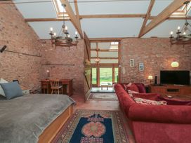 A living area with a bed, desk, red sofa, television, and stone walls at The Barn in Spaxton