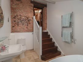 A bathroom with a toilet sink and stairs leading up with a brick wall and towel rack at The Barn in Spaxton