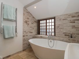 A bathroom with a freestanding bathtub near a window and a towel rack with two towels at The Barn in Spaxton