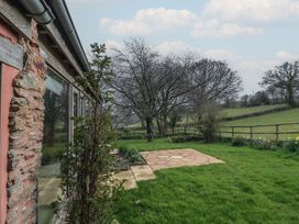 A garden with a stone patio and trees beside a stone and wood building at The Barn in Spaxton