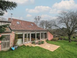 A backyard with green grass a leafless tree and a patio area outside a house with tiled roof and glass doors at The Barn in Spaxton