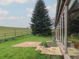A garden with grass a large evergreen tree and a stone patio next to a building with glass doors at The Barn in Spaxton