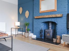 A living room with a blue brick fireplace and wood stove a plant on the floor and a lamp on a side table at Dolawen Bach in Conwy