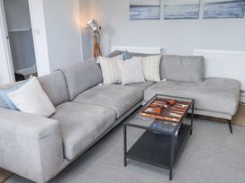 A living room with a gray sectional sofa and pillows a black glass coffee table with a backgammon set and game boxes on a gray rug at Dolawen Bach in Conwy