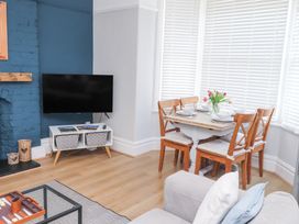 A dining area with a wooden table set for four next to a corner window with white blinds and a living area with a TV on a stand and a blue painted brick wall at Dolawen Bach in Conwy