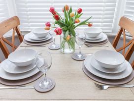 A dining table set with white plates bowls wine glasses cutlery and a vase of colorful tulips at Dolawen Bach in Conwy