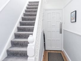 A hallway with a carpeted staircase a white door umbrella stand a wall picture and a floor mat at Dolawen Bach in Conwy