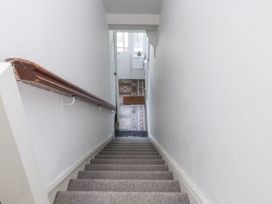 A staircase with carpet leading down to a hallway with patterned floor tiles and a door at Dolawen Bach in Conwy