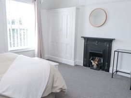 A bedroom with a bed beside a window a fireplace with a round mirror above and a small glass table at Dolawen Bach in Conwy